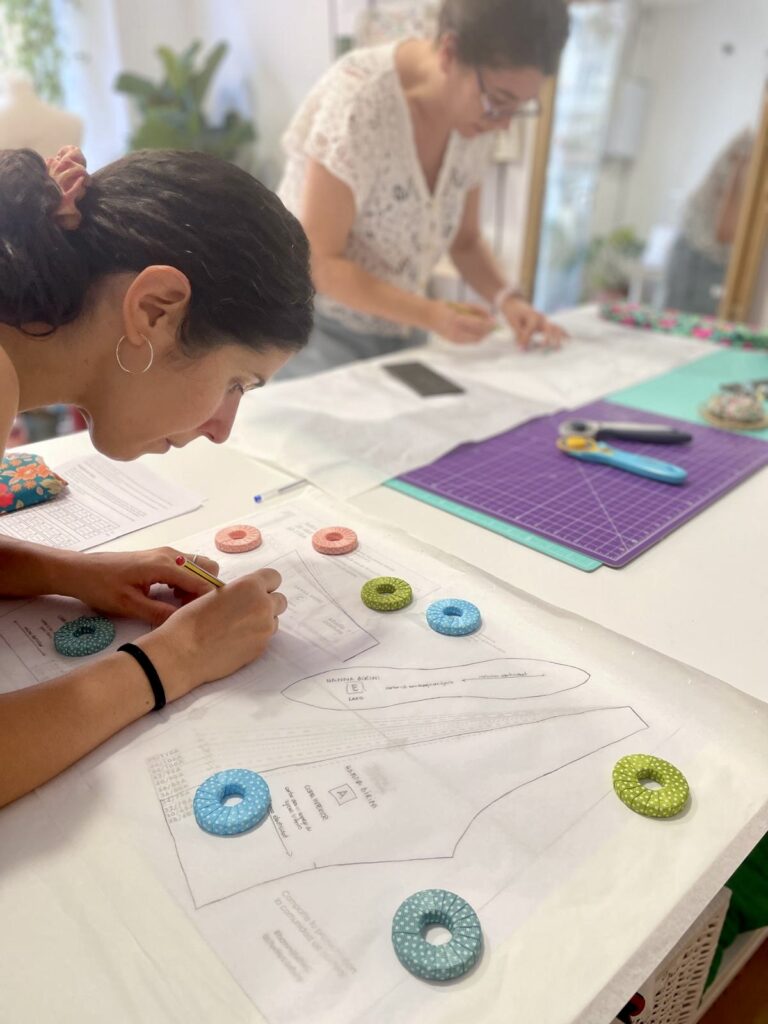 Alumnas aprendiendo a interpretar patrones en una clase de costura en Barcelona